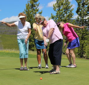 Four women are playing golf on a green.