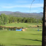 A view of a golf course with trees and water.