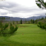 A golf course with trees and mountains in the background.